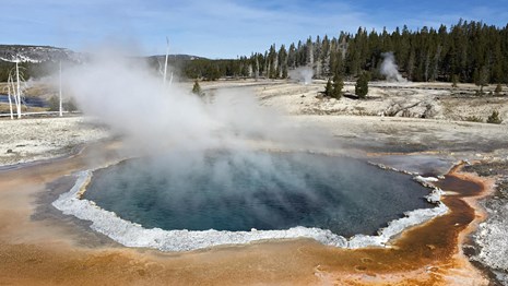 A round blue pool of hot water steams in a barren landscape.