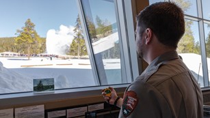 A ranger holds a stopwatch and times an erupting geyser.