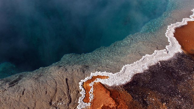 A dark blue hot spring with a white crested edge rimmed by orange water.