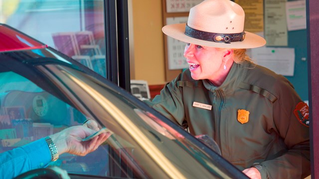 An entrance employee talks with a visitor in a vehicle.