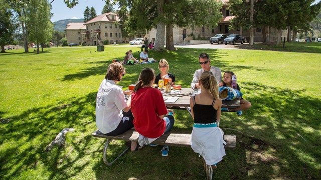 A family sits around a picnic table and enjoys a meal together.