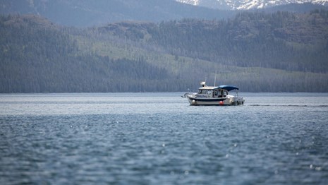 A motorboat on a large lake with snow-capped mountains in the background.