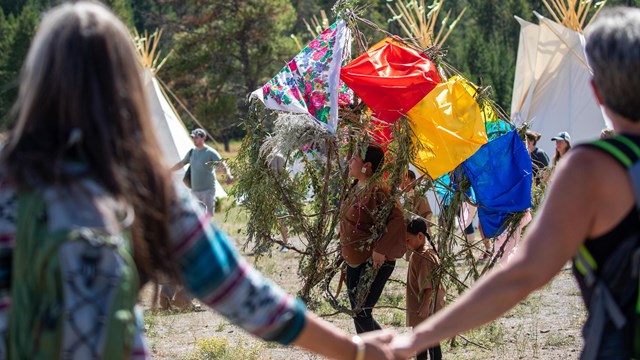 People dancing in Native regalia as onlookers hold hands