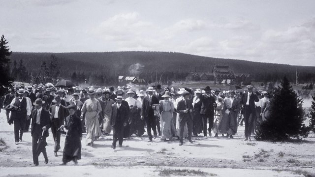 A historical photo of a group of people walking across a geyser runoff channel.