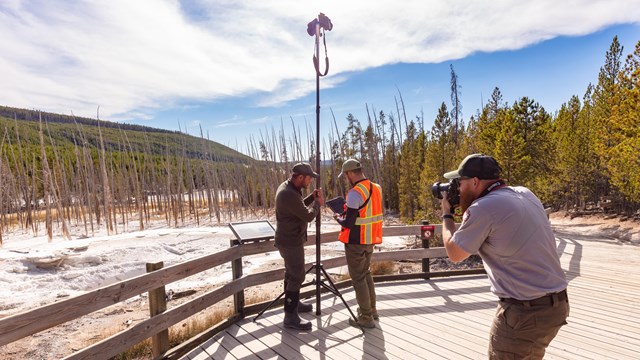 a park service employee photographing a team of geologists documenting a nearby thermal feature