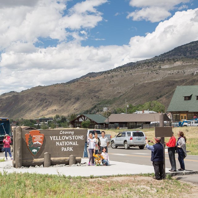 a group of people posing and smiling for a picture in front of a Yellowstone National Park sign