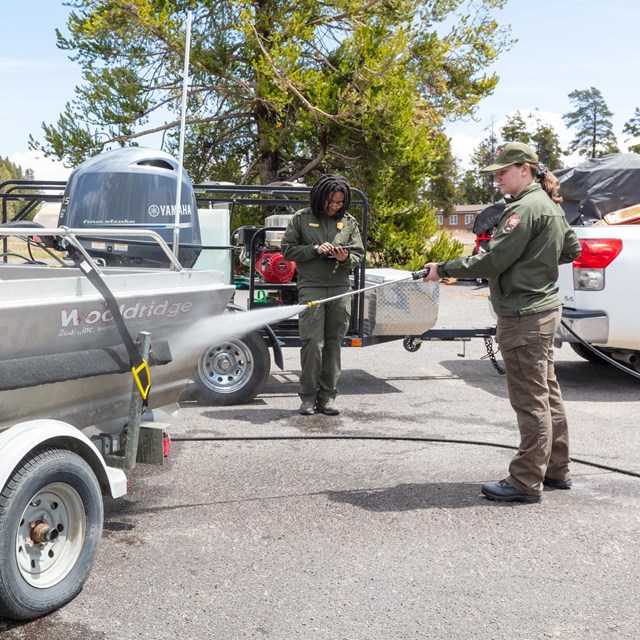 two park rangers conducting an AIS inspection and cleaning of a boat