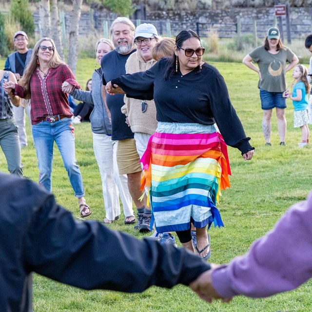 a group of people holding hands and dancing in a green field
