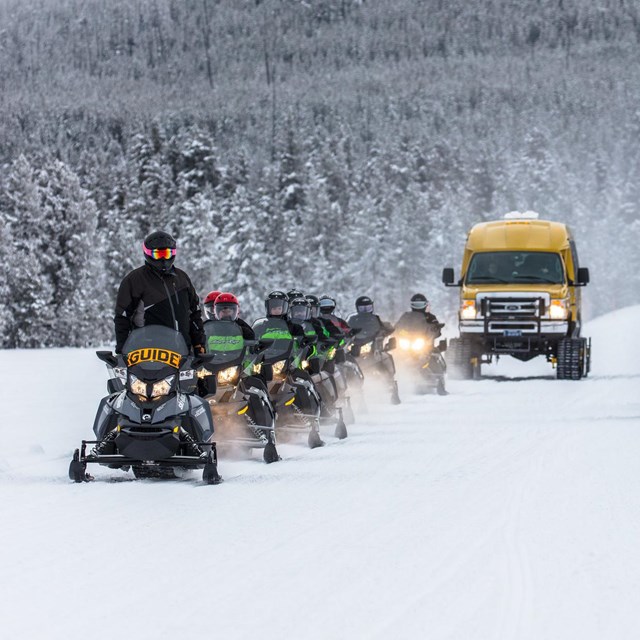 Snowmobiles and a snowcoach ride by a small group of bison