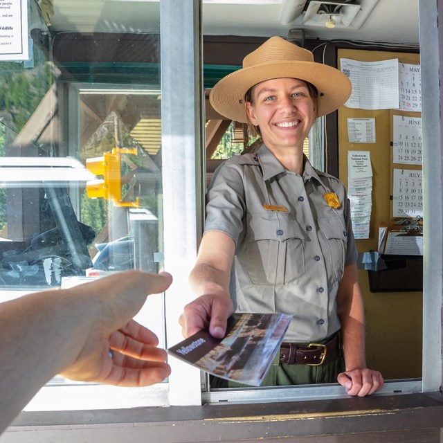 A park ranger smiling and handing someone a brochure at a park entrance