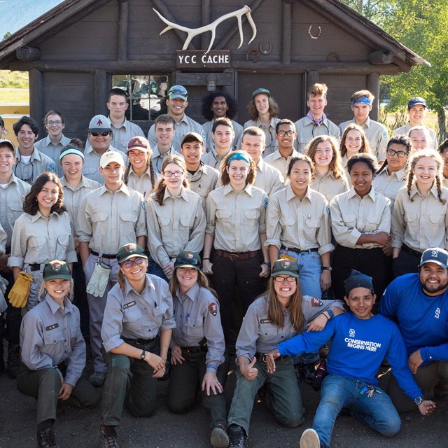 Students from around the country pose for a group photo in front of a wooden shed.
