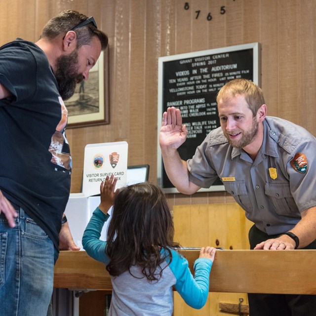A park ranger holds up his right hand to swear in a young junior ranger while a man looks on.