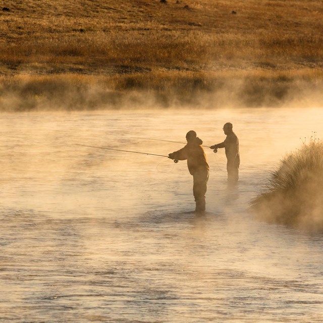 two people fishing in a river at sunrise as steam rises from the water