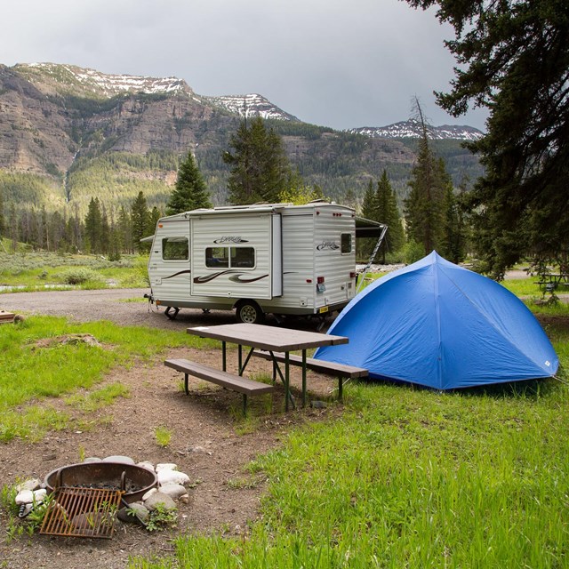 Campsite at Pebble Creek Campground with fire pit, picnic table, tent, and camper