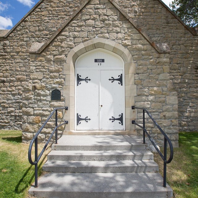 The grey stone chapel at Mammoth Hot Springs surrounded by green grass.