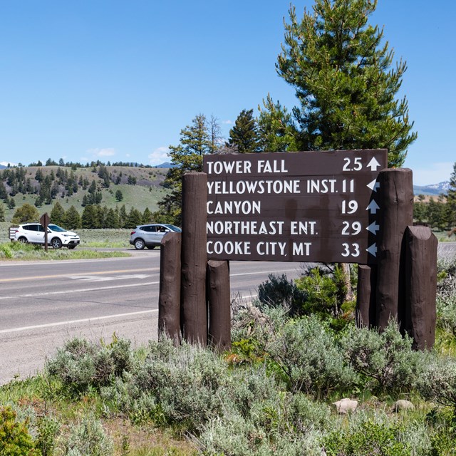 a large wooden sign near a roadway with points of interest and their distances away