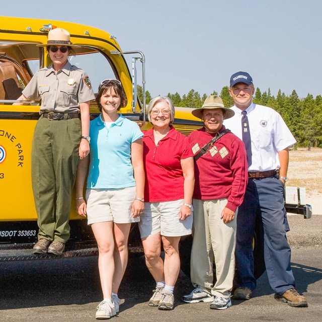 People posing alongside an historic yellow park bus.