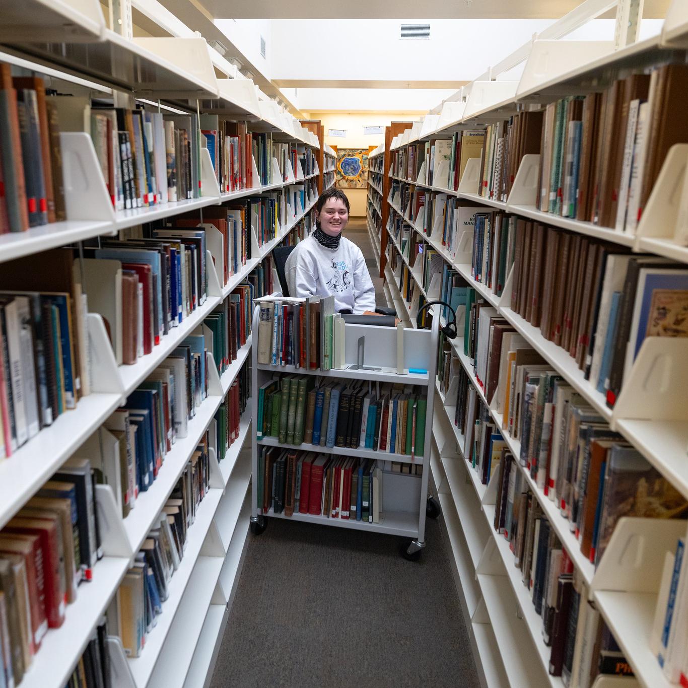 A person in a long aisle full of books in a library