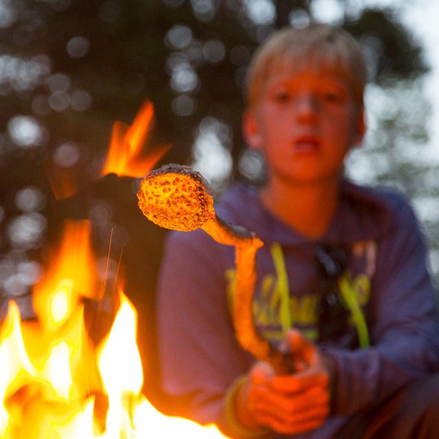 A camper toasts a marshmallow over an open fire