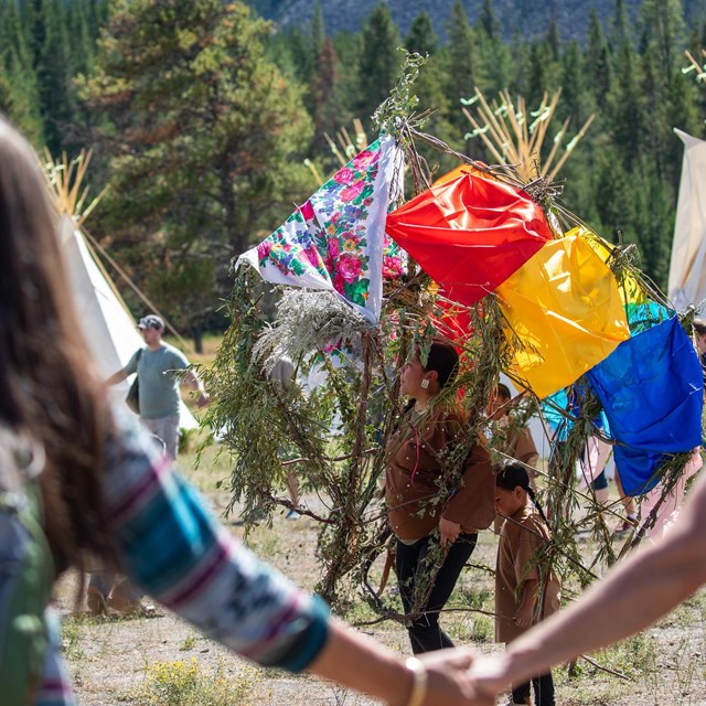 People dancing in Native regalia as onlookers hold hands