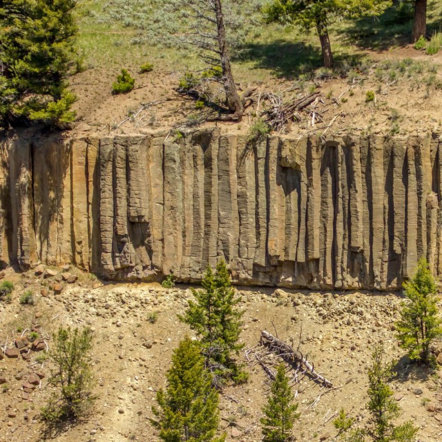 A rock formation made up of columns on the side of a gravelly hill
