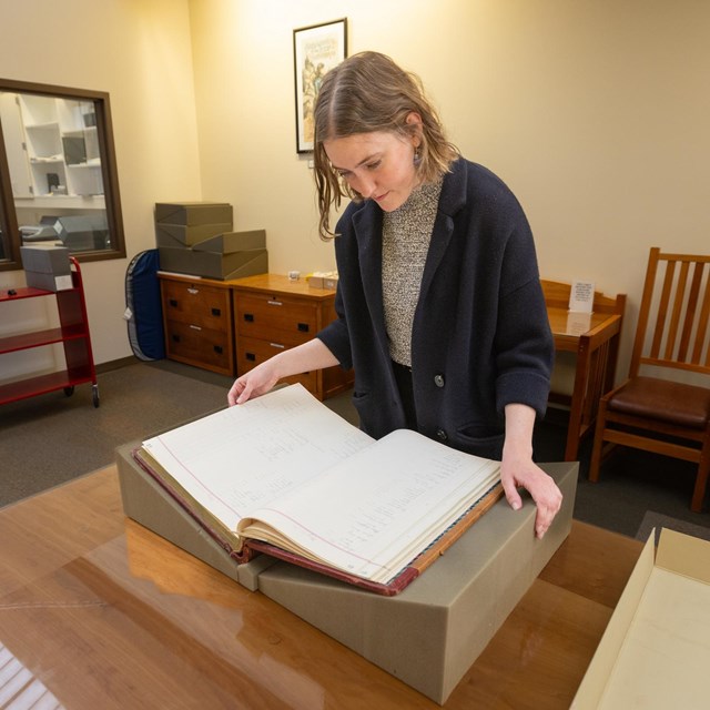 a woman reading a large book in a library