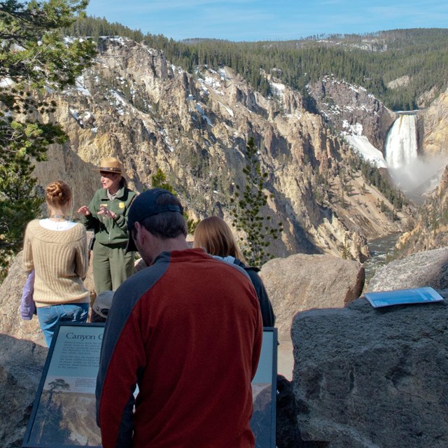 Ranger talking to a group of people with the Lower Falls in the background.
