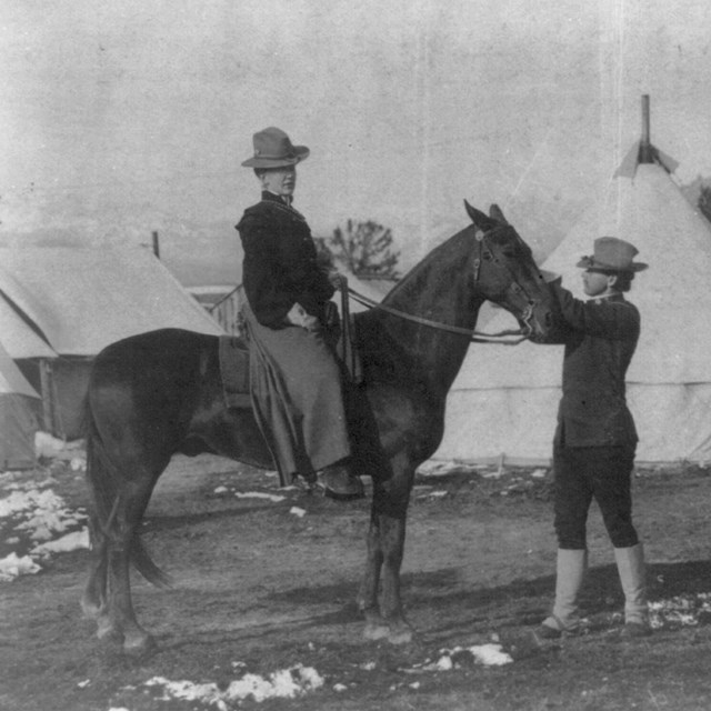 (U.S. soldier-guide holding woman's horse, African American trooper alongside, tents in background, 