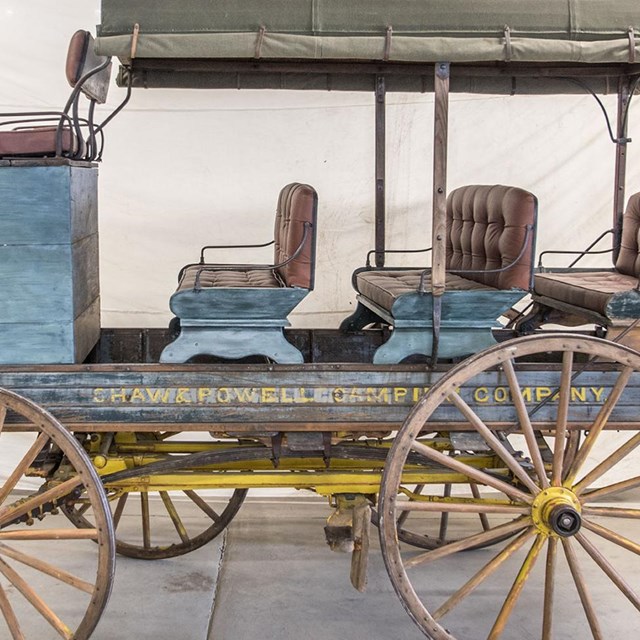 A painted Shaw and Powell Company wagon with a blue body, grey-green roof, yellow wheels.