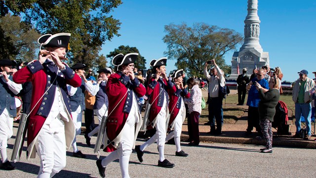 Fife and Drum wearing Red jackets play flutes in front of Victory Monument