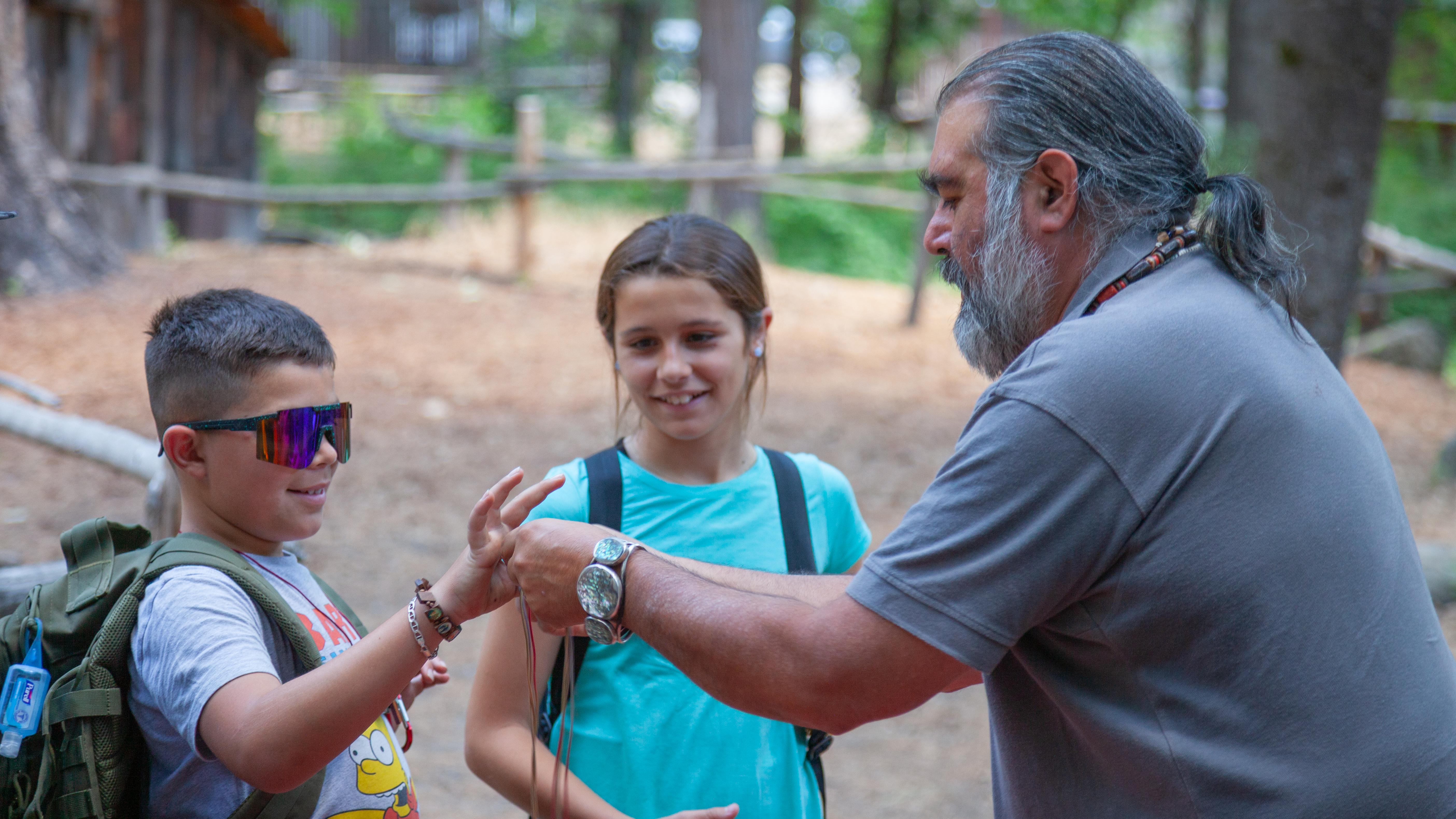 A bearded man holds out an item for two young children to examine.