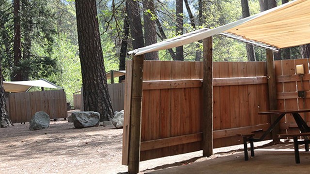 A brown wooden fence surrounds an open, canvas-topped unit at Housekeeping Camp.