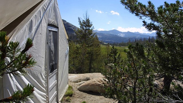 A white canvas-sided tent with a view of high country.