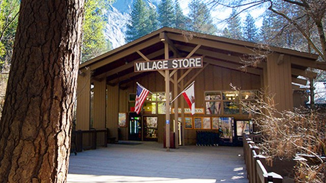 Exterior view of store entrance with large wood pillars and peaked roof, surrounded by trees.
