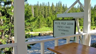 White "White Wolf" sign hanging from porch with forest and river views.