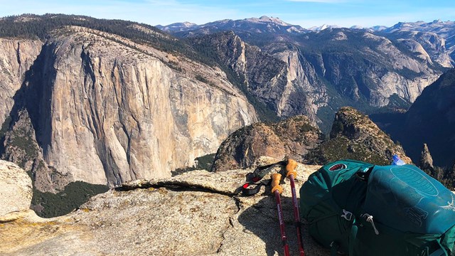 A backpack and trekking poles sit on a granite ledge overlooking Yosemite Valley