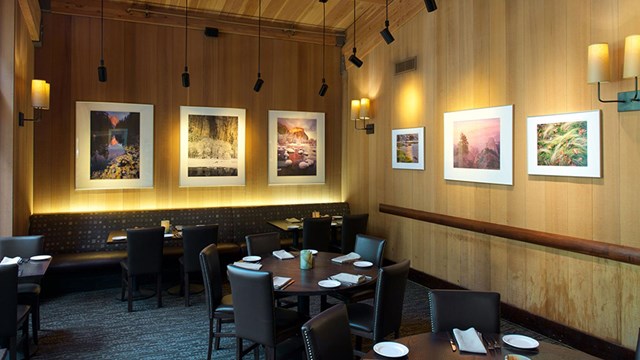 Wood-paneled dining room with round tables and sconce lighting.