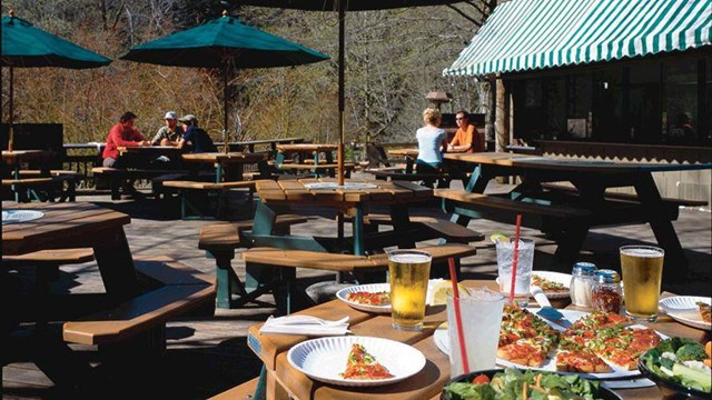 An outdoor table with pizza and drinks under a green umbrella.