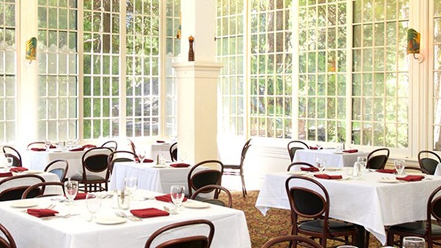 A bright dining area with white table cloths and wall-length windows.