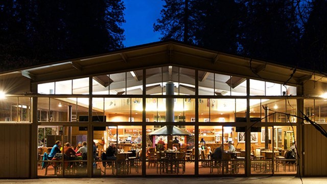 Outdoor view of lighted space at night, with tables and central fireplace.