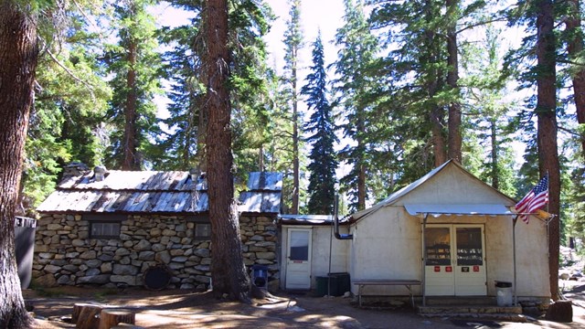 The exterior of a white-paneled and stone cottage under trees.