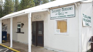 A white canvas-sided building with green signs reading "Tuolumne Meadows Grill"