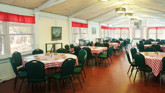 Interior of a white canvas-sided building, with round tables and red-checked tablecloths.