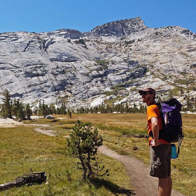 a person backpacking along a trail with a peak in the background