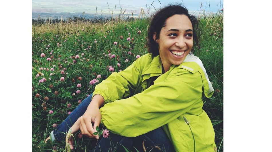 Young woman wearing a green windbreaker sits smiling in a field.