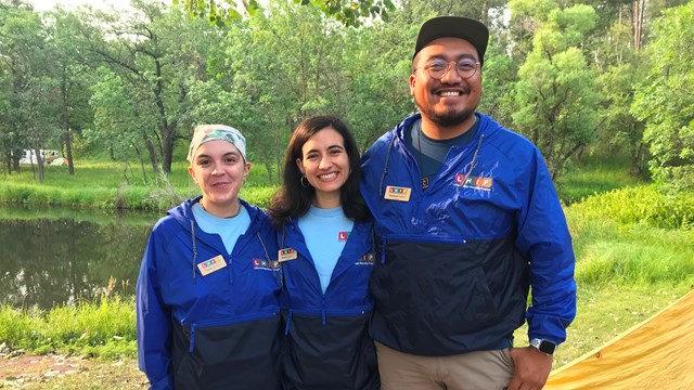 two women and a man posing for a picture smiling in the woods