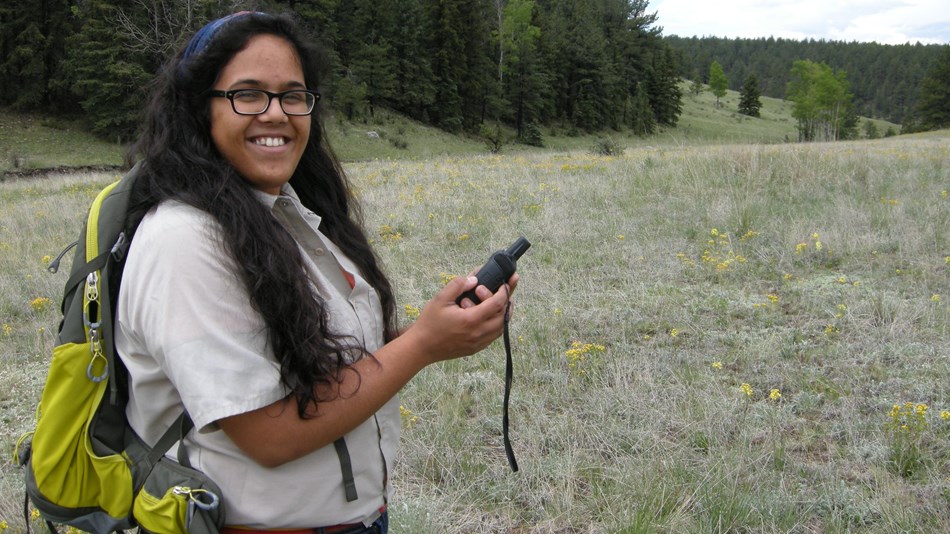 Young woman holding a GPS device while standing in a grass field