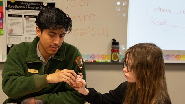 A ranger hands a piece of sandstone to a student in a classroom.