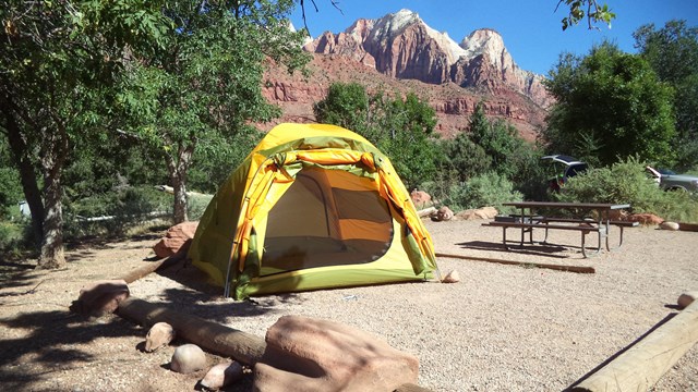 A tent on the ground next to a picnic table with red rock behind