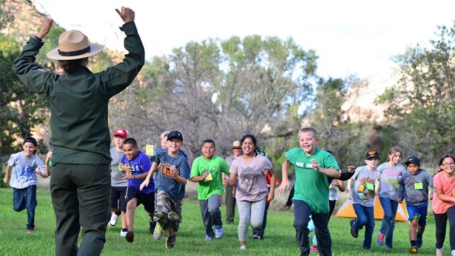 Group of smiling children runs toward park ranger as part of a school program.
